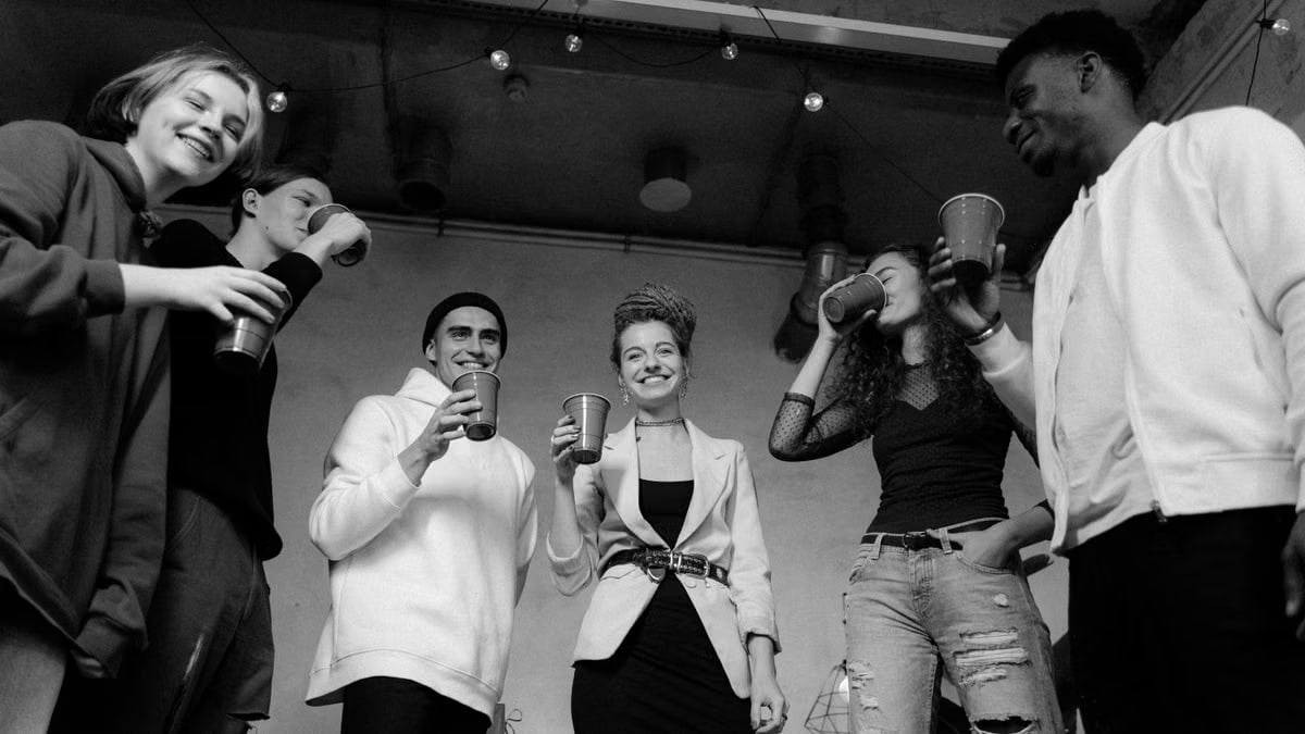 A group of diverse young adults enjoying a lively indoor party in black and white.